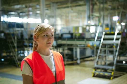 Portrait of a female employee in an orange robe vest in the working space of a production facility, supervises and controls the line in food production, against the background of equipment