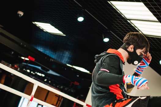 Professional Muay Thai fighter. Male boxer in training sportswear, an exercise in sports hall, fight with a shadow in ring, Strike testing in sports mask