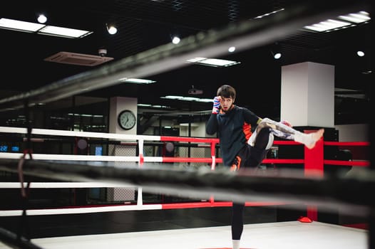 Professional Muay Thai fighter. Male boxer in training sportswear, an exercise in sports hall, fight with a shadow in ring, Strike testing