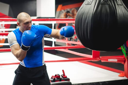 Professional Muay Thai fighter. Male boxer in training sportswear, an exercise in sports hall, Training with a punching bag, working out blows