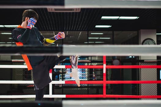 Professional Muay Thai fighter. Male boxer in training sportswear, an exercise in sports hall, fight with a shadow in ring, Strike testing