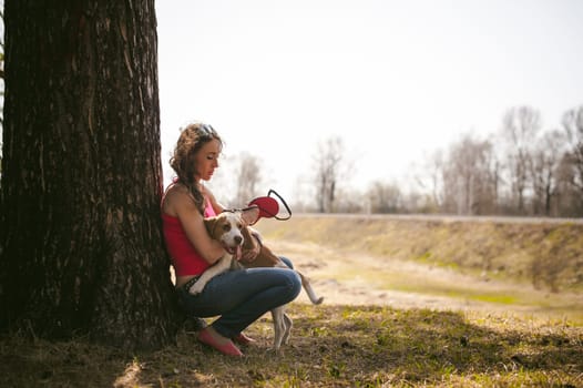 Young pet dog breeds beagle walking in park outdoors. woman carefully walks puppy, plays and tranitsiruetsya, sits with pet in an embrace under tree on grass in woods in clearing