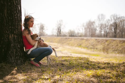 Young pet dog breeds beagle walking in park outdoors. woman carefully walks puppy, plays and tranitsiruetsya, sits with pet in an embrace under tree on grass in woods in clearing