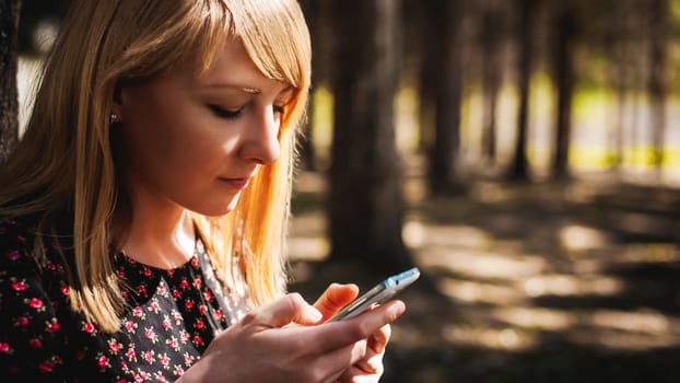 blonde woman dressed summer dress, black pantyhose and sneakers with white sole, resting nature enjoying warm sunny day. Sits under tree alone, holding in hand cell phone, Emotion online communication