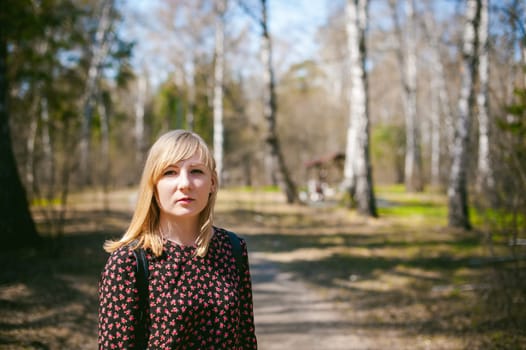Portrait of a blonde woman in dress walking through forest park against background