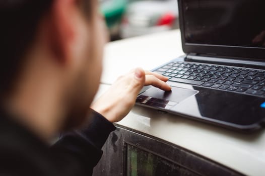 man with a laptop in parking lot in yard near car is doing manipulations with cyber system, concept
