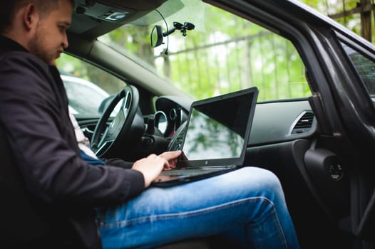 Professional man with a laptop in car tunes tuning control system, updating software, gaining access through to computer, sitting in cabin