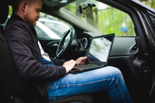 Professional man with a laptop in car tunes tuning control system, updating software, gaining access through to computer, sitting in cabin