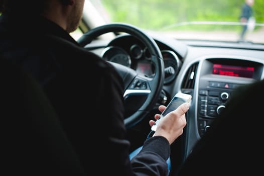Man at the wheel of a car holds a phone in his hand