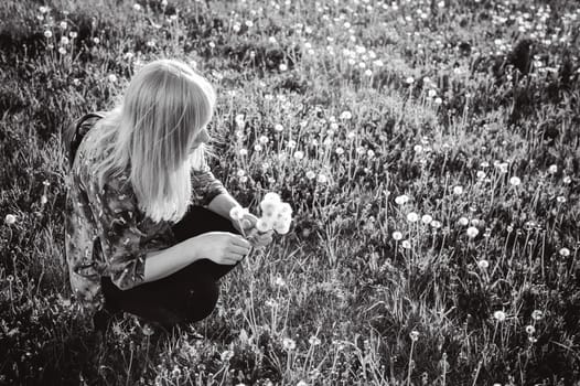 Young blonde girl in dress with shoulder bag, walking on dandelion field, against background of urban architecture, breathing relaxing in cityscape