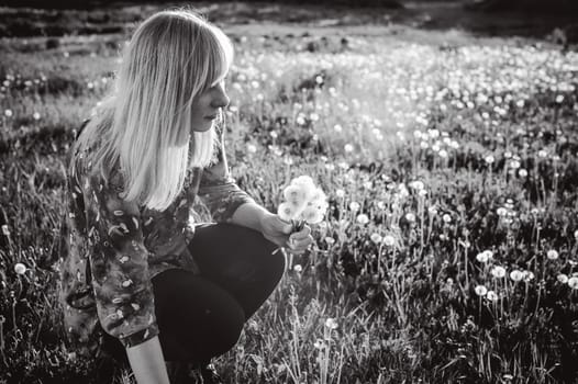 Young blonde girl in dress with shoulder bag, walking on dandelion field, against background of urban architecture, breathing relaxing in cityscape