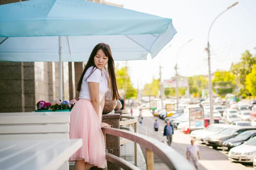 Cute asian young woman in summer cafe outdoors. girl In white T-shirt, with long hair in simple light cozy interior of restaurant Urban style