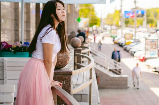 Cute asian young woman in summer cafe outdoors. girl In white T-shirt, with long hair in simple light cozy interior of restaurant Urban style