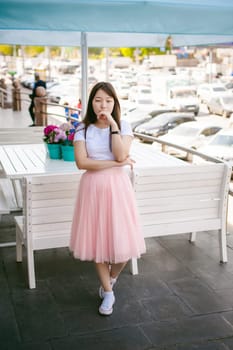 Cute asian young woman in summer cafe outdoors. girl In white T-shirt, with long hair in simple light cozy interior of restaurant Urban style