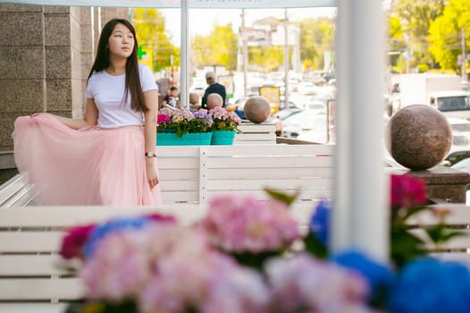 Cute asian young woman in summer cafe outdoors. girl In white T-shirt, with long hair in simple light cozy interior of restaurant Urban style