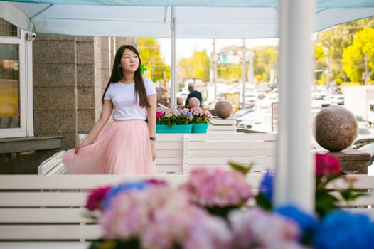 Cute asian young woman in summer cafe outdoors. girl In white T-shirt, with long hair in simple light cozy interior of restaurant Urban style