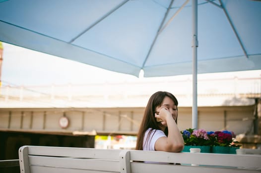 Cute asian young woman in summer cafe outdoors. girl In white T-shirt, with long hair in simple light cozy interior of restaurant Urban style, Communicates on a cell phone holding it in his hands