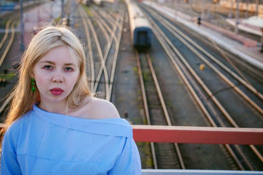 portrait of a cute young blond woman in a summer day against the background of a railway station