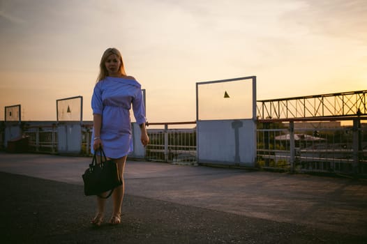 portrait of a cute young blond woman in a summer day against the background of a railway station