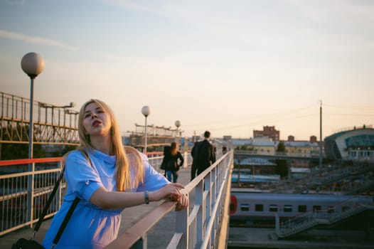 portrait of a cute young blond woman in a summer day against the background of a railway station