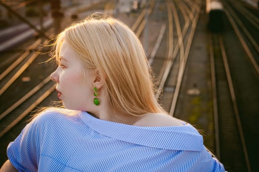 portrait of a cute young blond woman in a summer day against the background of a railway station
