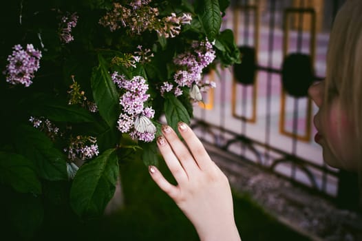female fingers hold white butterflies on flowers of lilac and green leaves