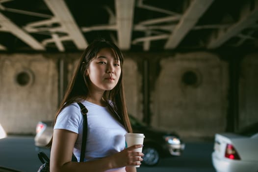 Cute asian young woman with a glass of takeaway, walks in an urban environment
