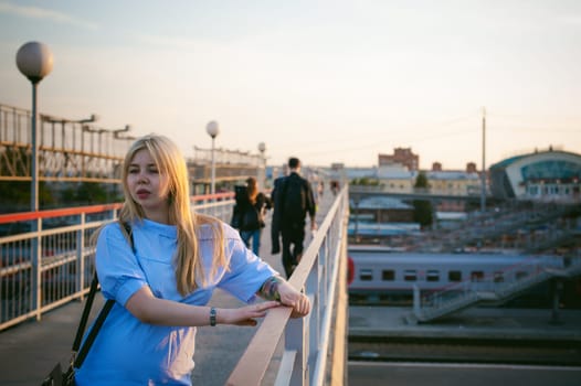 portrait of a cute young blond woman in a summer day against the background of a railway station