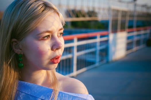 portrait of a cute young blond woman in a summer day against the background of a railway station