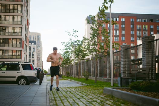 Handsome sexy male bodybuilder athlete man with naked torso, running in morning, outdoors. Healthy lifestyle concept.