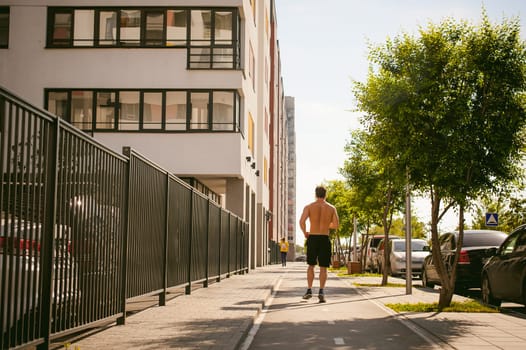 Handsome sexy male bodybuilder athlete man with naked torso, Morning run in open air in urban courtyards, early sunny summer morning. Healthy lifestyle concept.