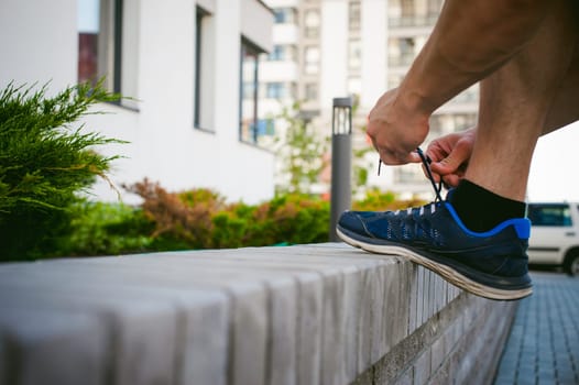 Handsome sexy male bodybuilder athlete man with naked torso, running in morning, outdoors. ties up shoelaces on sneakers. Healthy lifestyle concept.