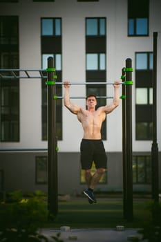 Handsome sexy male bodybuilder athlete man doing crossfit workout in athletic facilities on sunny morning outdoors. Healthy lifestyle concept. Physical preparation of body. pull-up on horizontal bar