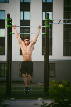 Handsome sexy male bodybuilder athlete man doing crossfit workout in athletic facilities on sunny morning outdoors. Healthy lifestyle concept. Physical preparation of body. pull-up on horizontal bar