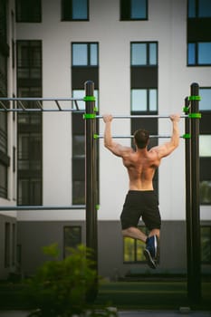 Handsome sexy male bodybuilder athlete man doing crossfit workout in athletic facilities on sunny morning outdoors. Healthy lifestyle concept. Physical preparation of body. pull-up on horizontal bar