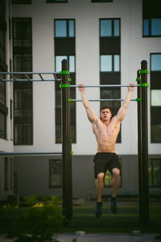 Handsome sexy male bodybuilder athlete man doing crossfit workout in athletic facilities on sunny morning outdoors. Healthy lifestyle concept. Physical preparation of body. pull-up on horizontal bar