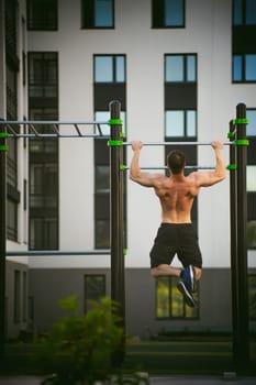 Handsome sexy male bodybuilder athlete man doing crossfit workout in athletic facilities on sunny morning outdoors. Healthy lifestyle concept. Physical preparation of body. pull-up on horizontal bar