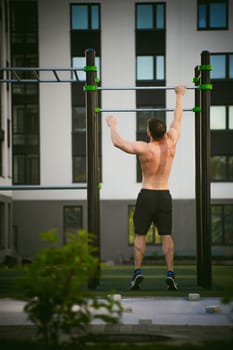 Handsome sexy male bodybuilder athlete man doing crossfit workout in athletic facilities on sunny morning outdoors. Healthy lifestyle concept. Physical preparation of body. pull-up on horizontal bar