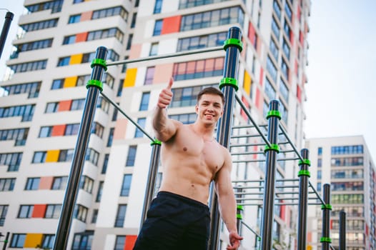 Handsome sexy male bodybuilder athlete man doing crossfit workout in athletic facilities on sunny morning outdoors. Healthy lifestyle concept. Physical preparation of body. Model showing Thumbs up