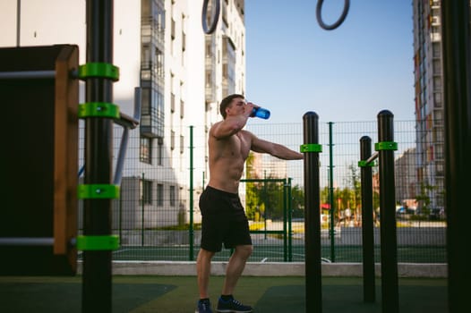 Handsome sexy male bodybuilder athlete man doing crossfit workout in athletic facilities on sunny morning outdoors. Healthy lifestyle concept. Rest after exercise.