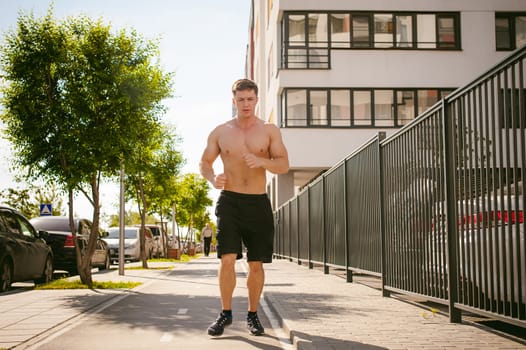 Handsome sexy male bodybuilder athlete man with naked torso, Morning run in open air in urban courtyards, early sunny summer morning. Healthy lifestyle concept.
