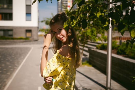 Young beautiful woman is strolling outdoors in the yard, against the backdrop of greenery and houses, warm summer sunny day