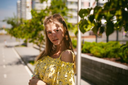 Young beautiful woman is strolling outdoors in the yard, against the backdrop of greenery and houses, warm summer sunny day