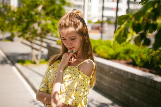 Young beautiful woman is strolling outdoors in the yard, against the backdrop of greenery and houses, warm summer sunny day