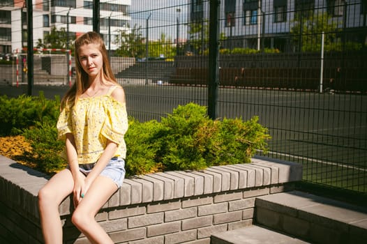 Young beautiful woman is strolling outdoors in the yard, against the backdrop of greenery and houses, warm summer sunny day