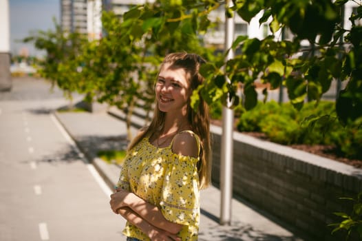 Young beautiful woman is strolling outdoors in the yard, against the backdrop of greenery and houses, warm summer sunny day