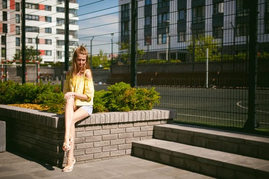 Young beautiful woman is strolling outdoors in the yard, against the backdrop of greenery and houses, warm summer sunny day