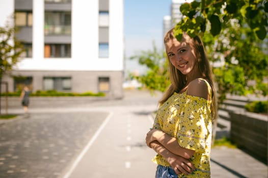 Young beautiful woman is strolling outdoors in the yard, against the backdrop of greenery and houses, warm summer sunny day