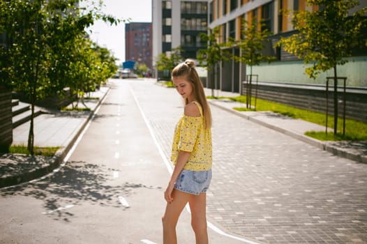 Young beautiful woman is strolling outdoors in the yard, against the backdrop of greenery and houses, warm summer sunny day