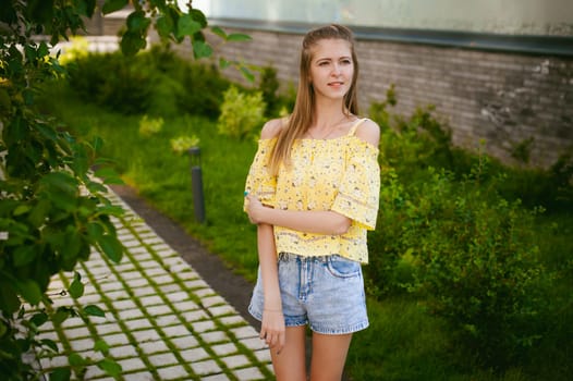 Young beautiful woman is strolling outdoors in the yard, against the backdrop of greenery and houses, warm summer sunny day